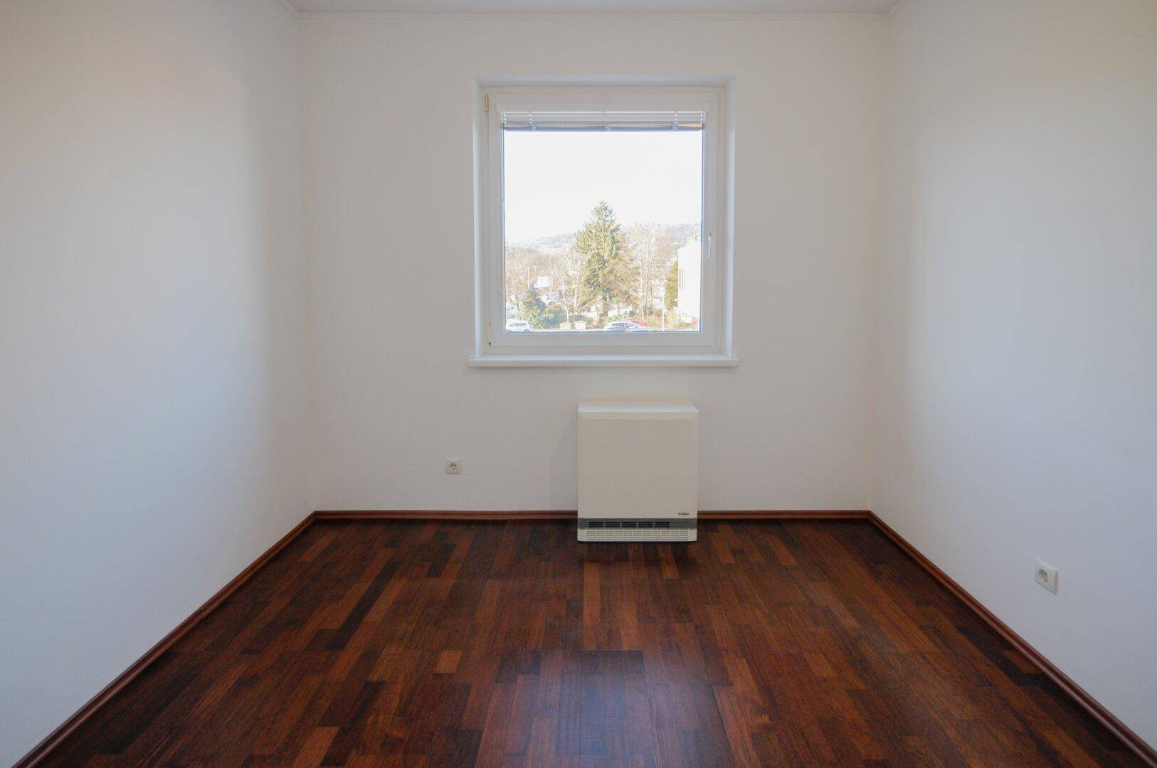 Ruhiges Zimmer mit dunklem Parkettboden und einem Fenster, das eine angenehme Atmosphäre schafft.