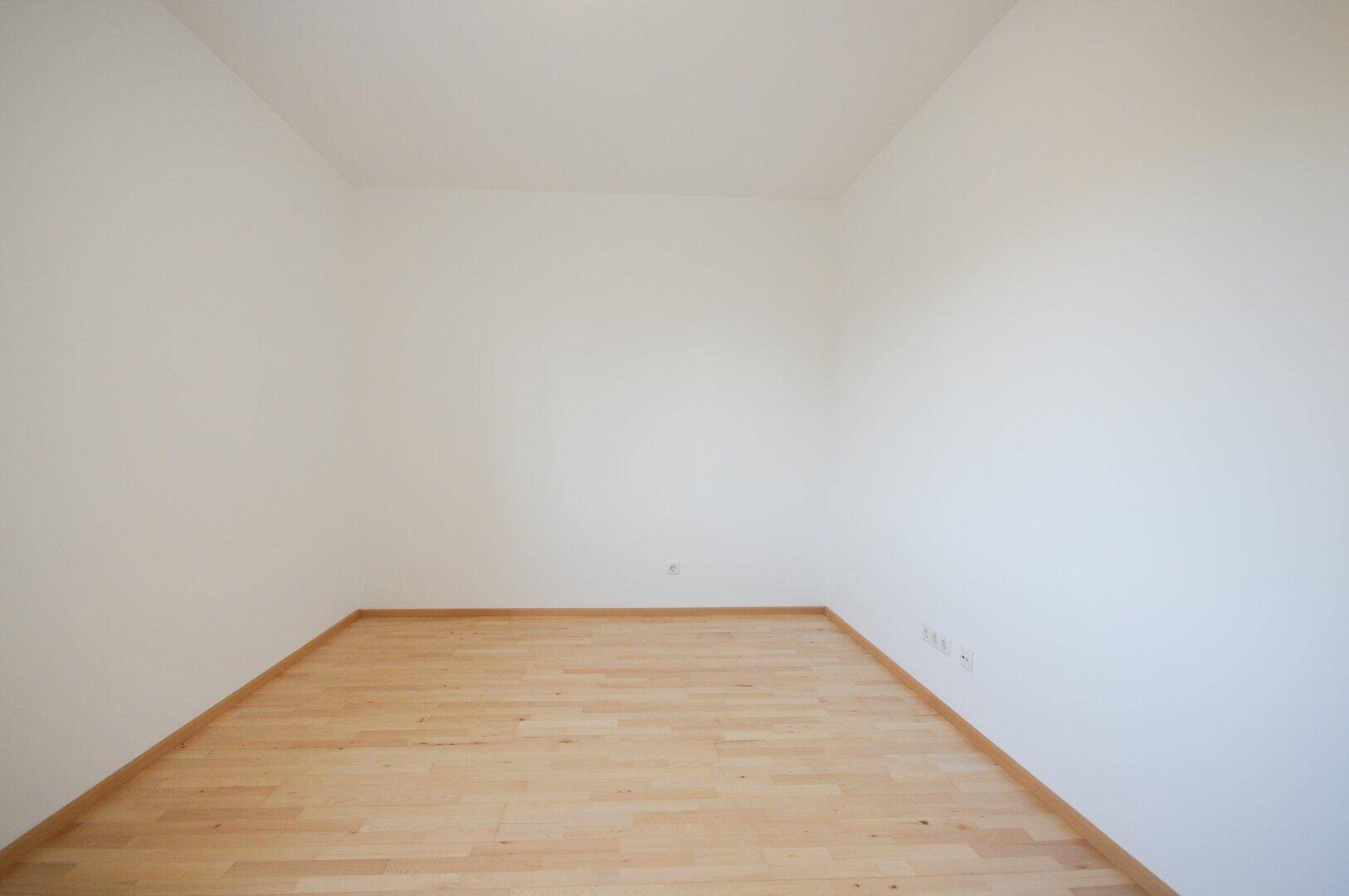 Leeres Zimmer mit hellem Parkettboden und weißen Wänden, bereit für neue Bewohner.