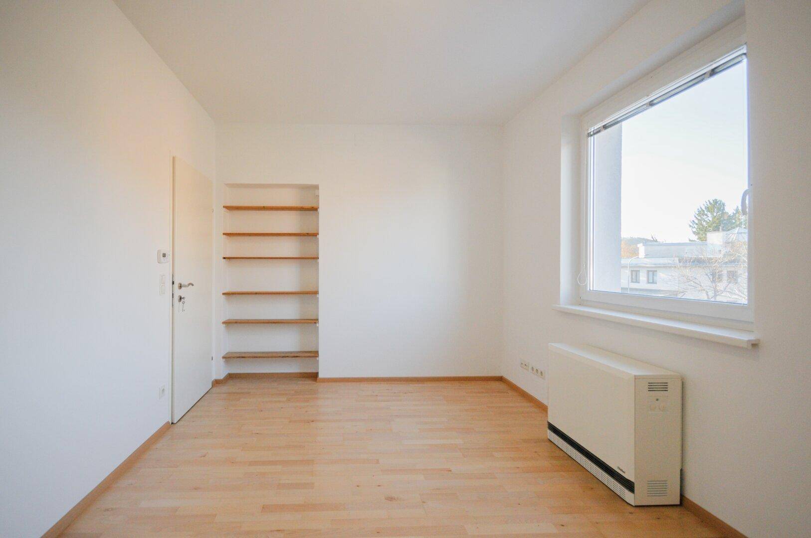 Helles Zimmer mit Parkettboden und eingebauten Regalen, ideal als Kinder- oder Arbeitszimmer.