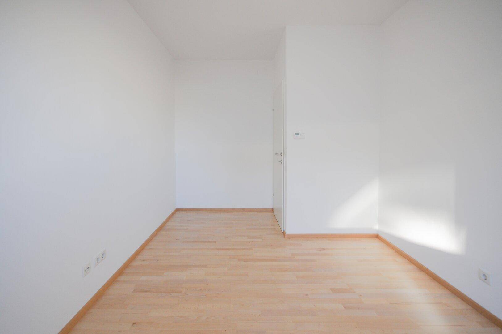Leeres Zimmer mit hellem Parkettboden und weißen Wänden, das viel Gestaltungspotenzial bietet.