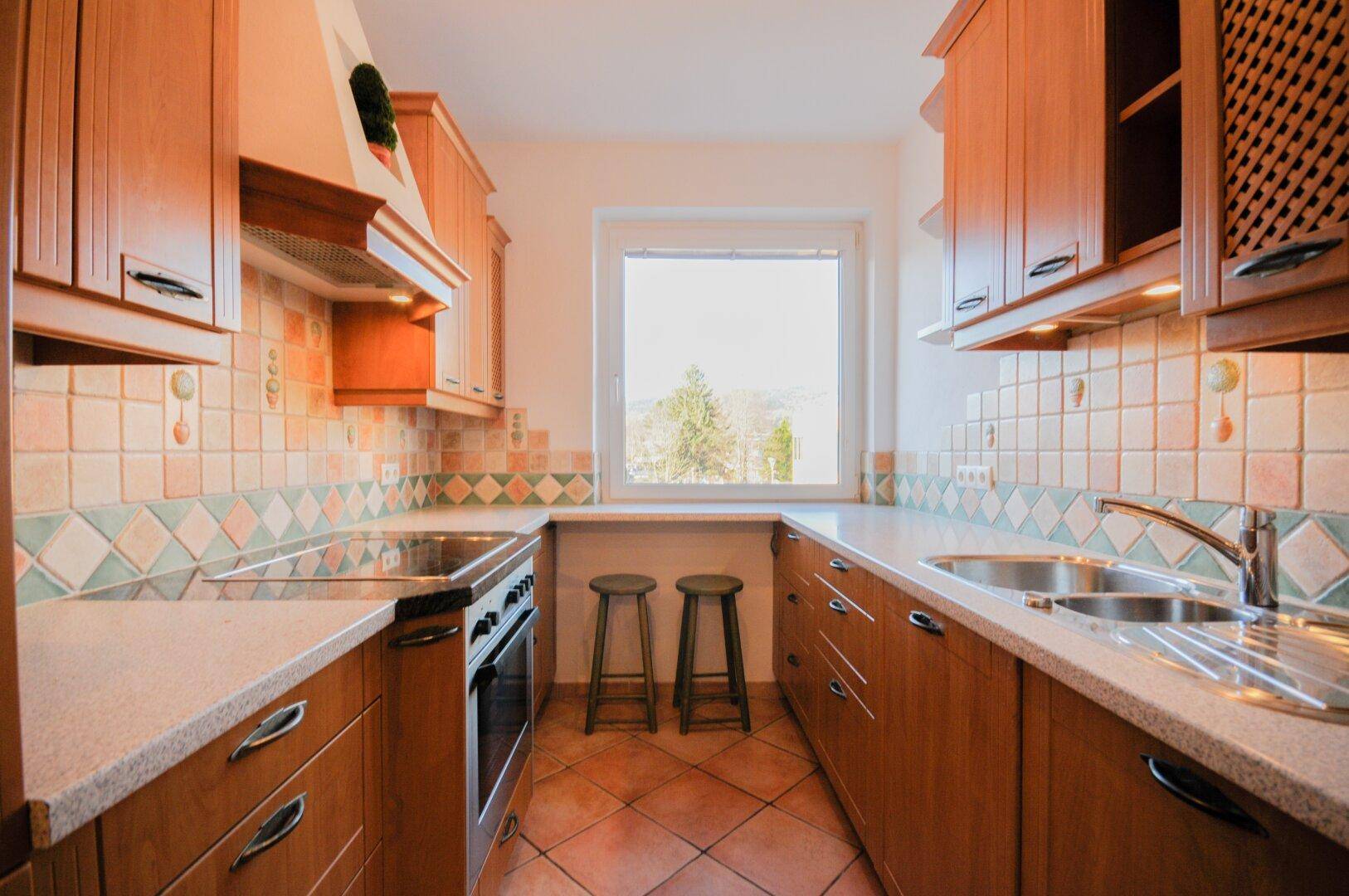 Traditionelle Küche mit Holzschränken, Terrakotta-Fliesen und Fenster mit Blick ins Grüne.