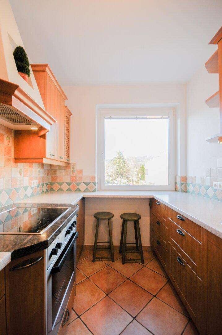 Helle Küche mit Holzschränken, Terrakotta-Fliesen und einem Fenster, das viel Tageslicht hereinlässt.