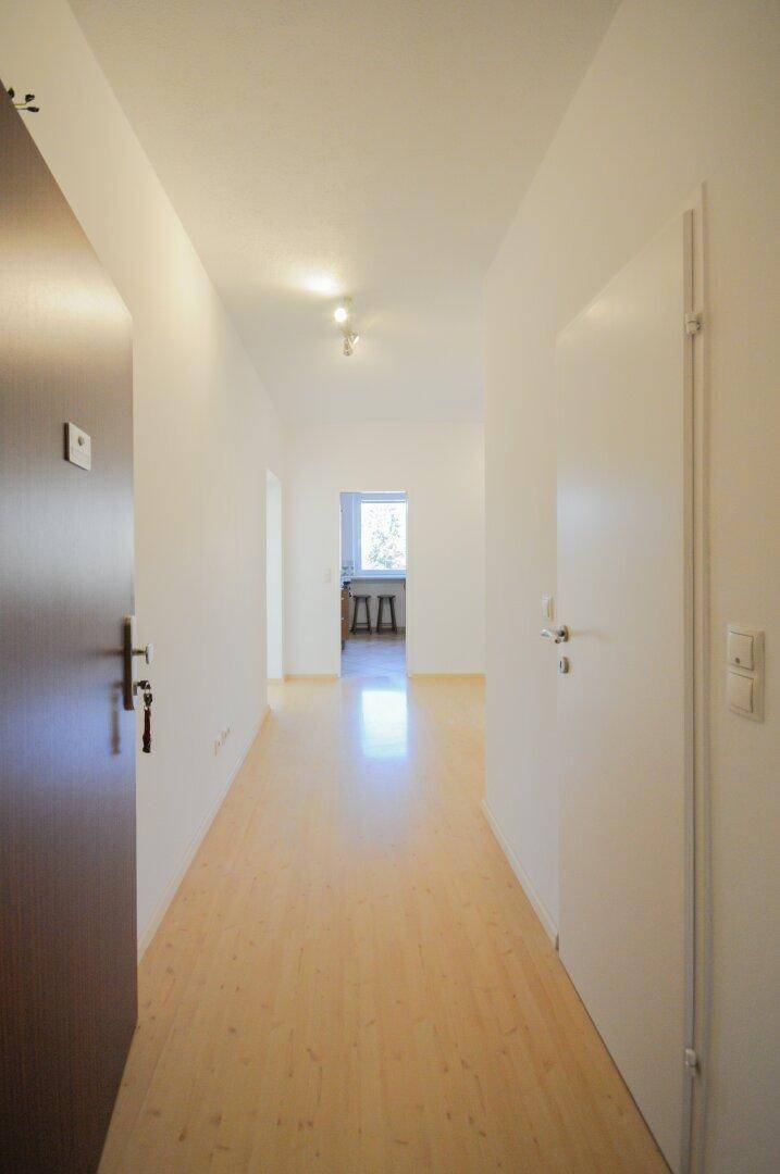 Langer, heller Flur mit Parkettboden, der zu den verschiedenen Räumen der Wohnung führt.