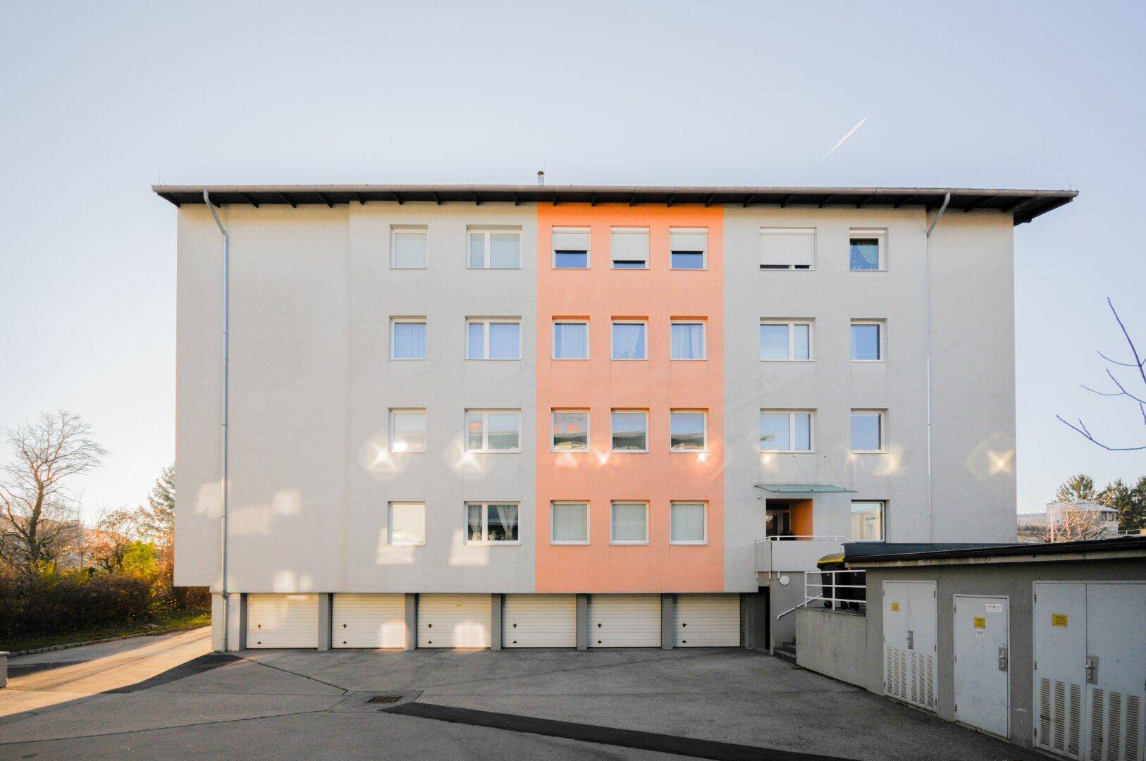 Mehrfamilienhaus mit Garagen im Erdgeschoss und einer farblich abgesetzten Fassade.