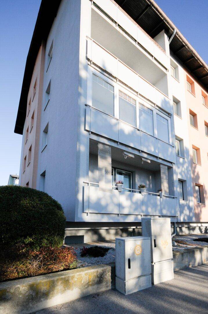 Seitenansicht des Mehrfamilienhauses mit Balkonen und einem gepflegten Vorgartenbereich.