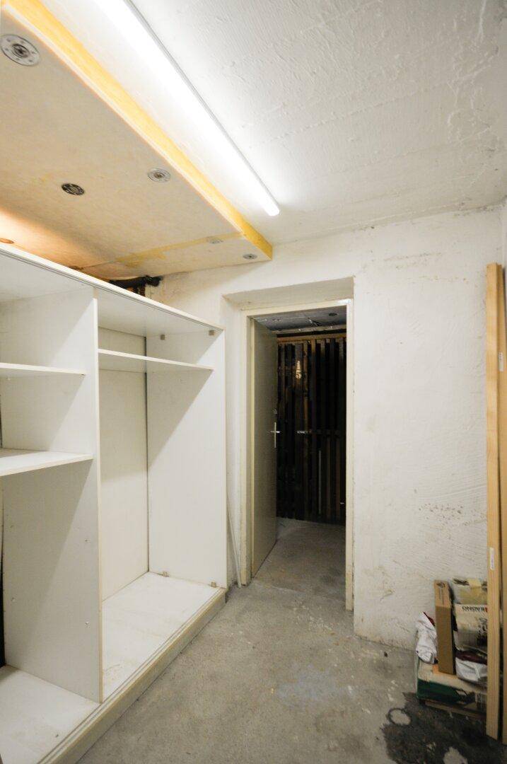 Kellerabteil mit Regalen und einer Tür, die zu weiteren Lagerräumen führt.