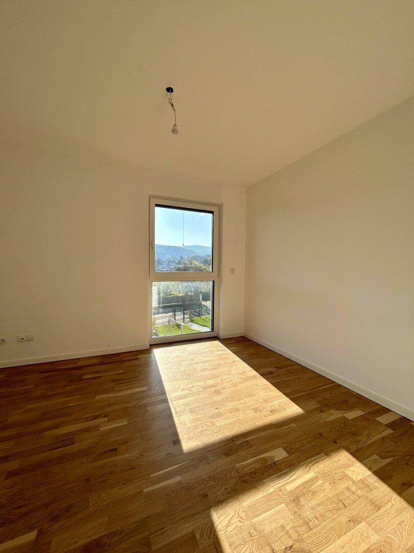 Helles Schlafzimmer mit Holzboden und großem Fenster, das viel Tageslicht hereinlässt.