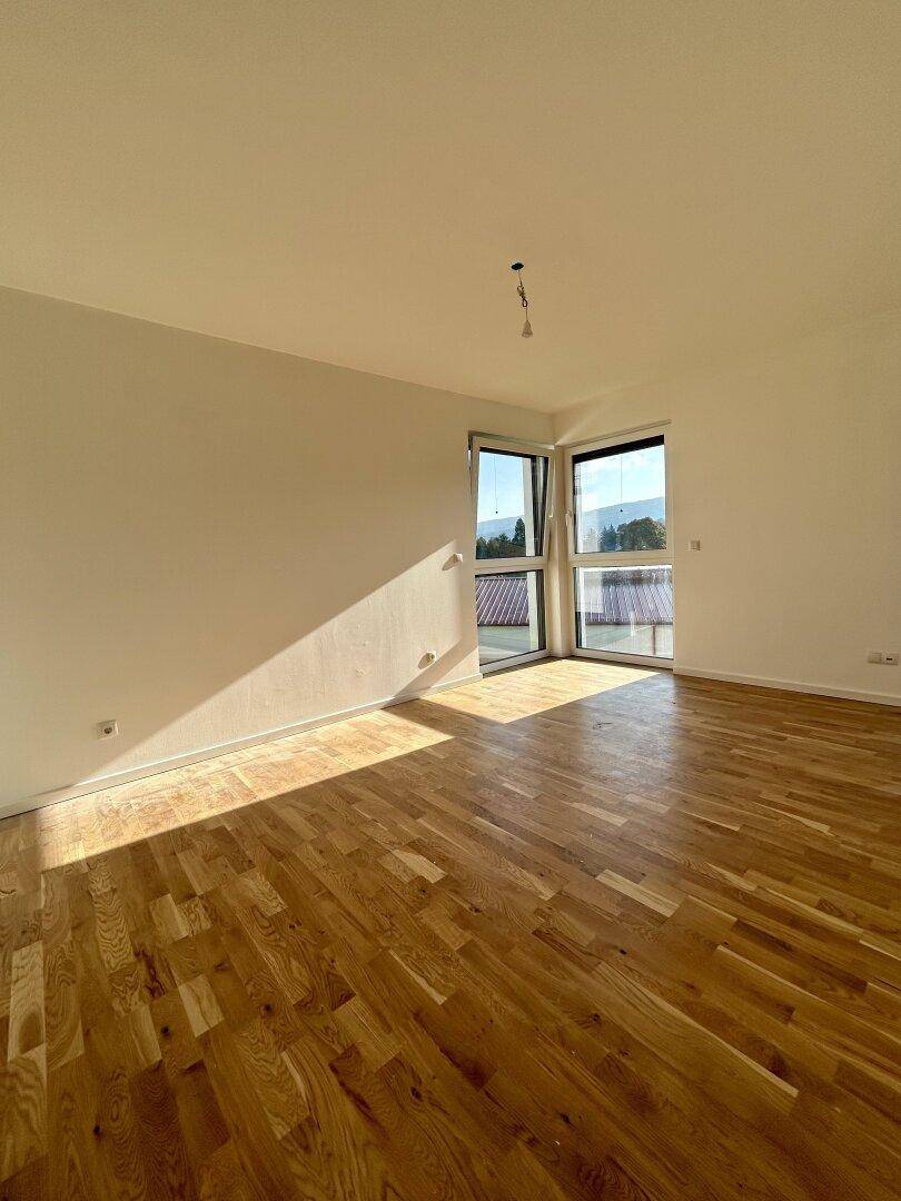 Sonniger Raum mit Holzboden und Eckfenstern, die einen weiten Blick bieten.