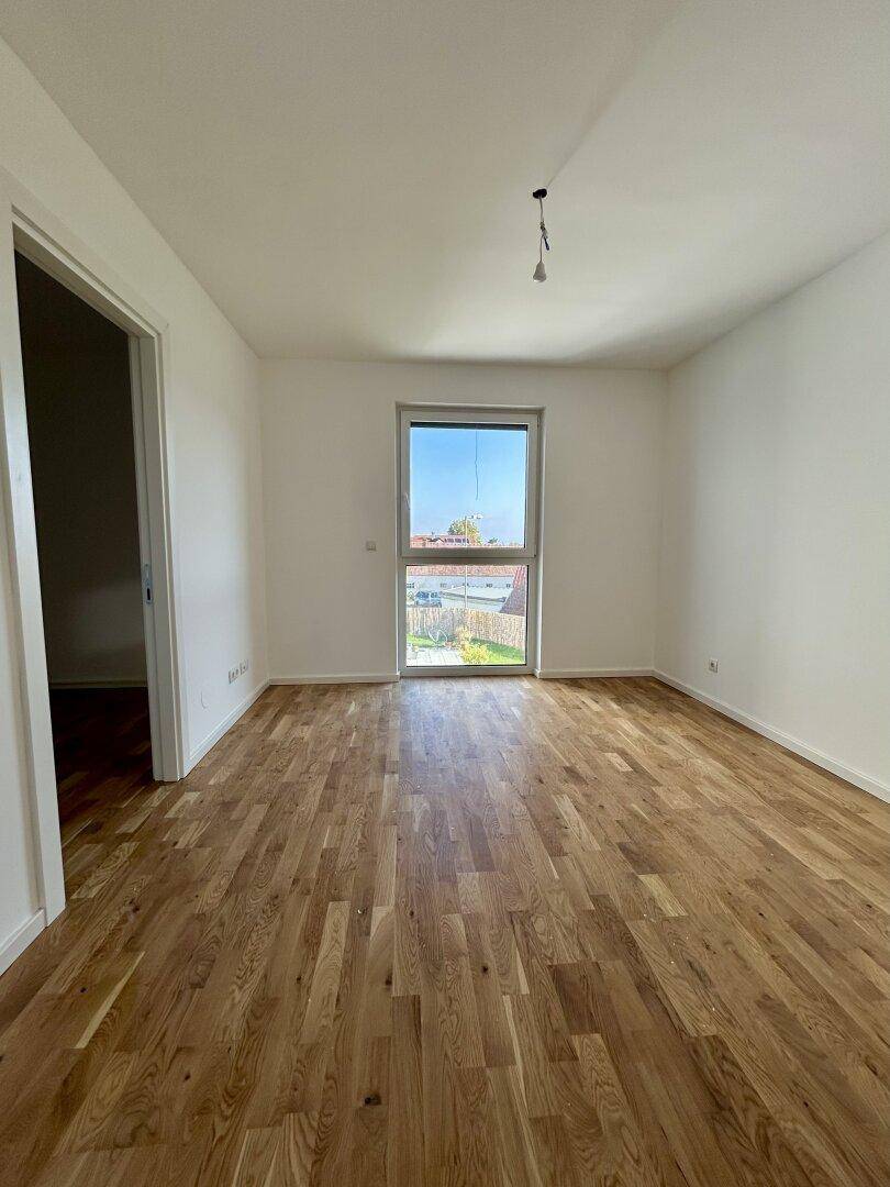 Heller Raum mit Holzboden und Fenster, das den Blick auf den Garten freigibt.
