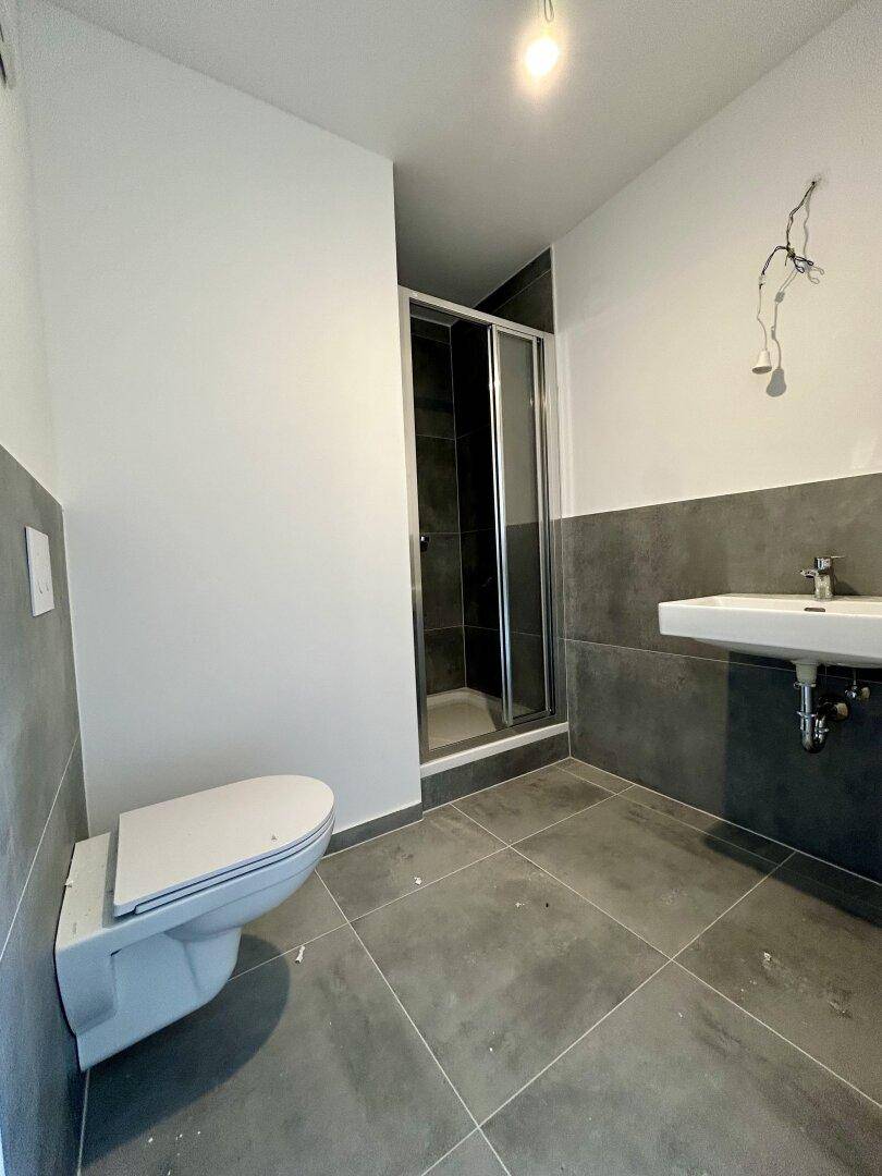 Modernes Badezimmer mit grauen Fliesen, Dusche und wandhängendem WC.
