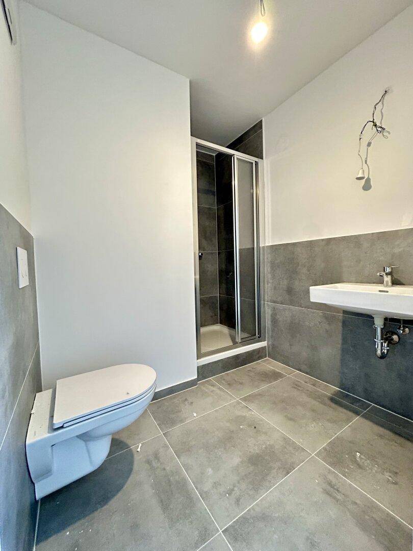 Modernes Badezimmer mit grauen Fliesen, Dusche und wandhängendem WC.