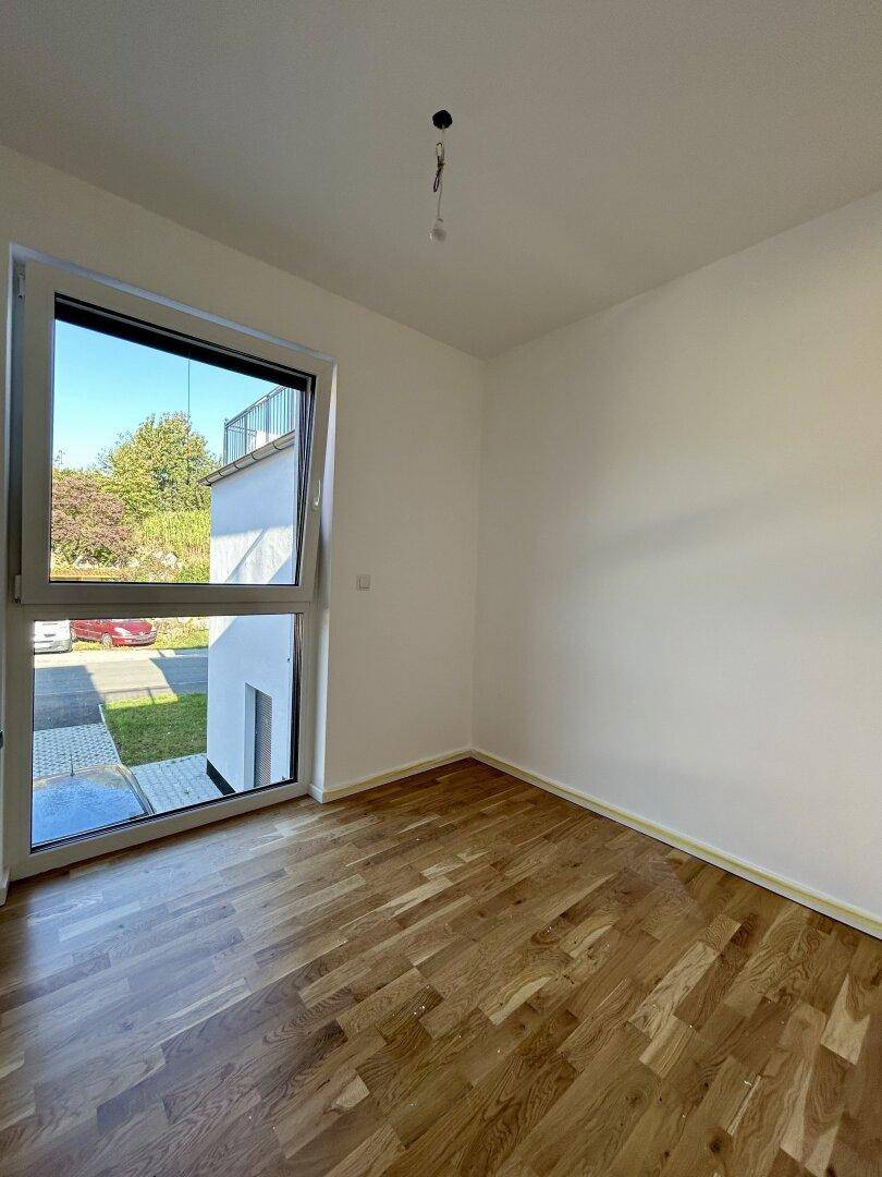 Heller Raum mit Holzboden und großem Fenster, das viel Tageslicht hereinlässt.