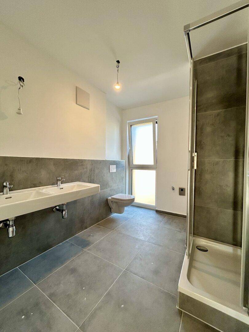 Geräumiges Badezimmer mit Doppelwaschbecken, Dusche und Fenster für Tageslicht.