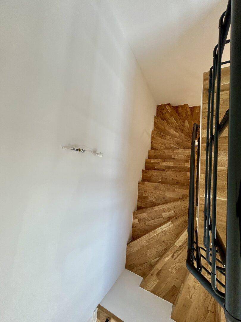 Holztreppe mit schwarzem Geländer, die die oberen Etagen des Hauses verbindet.