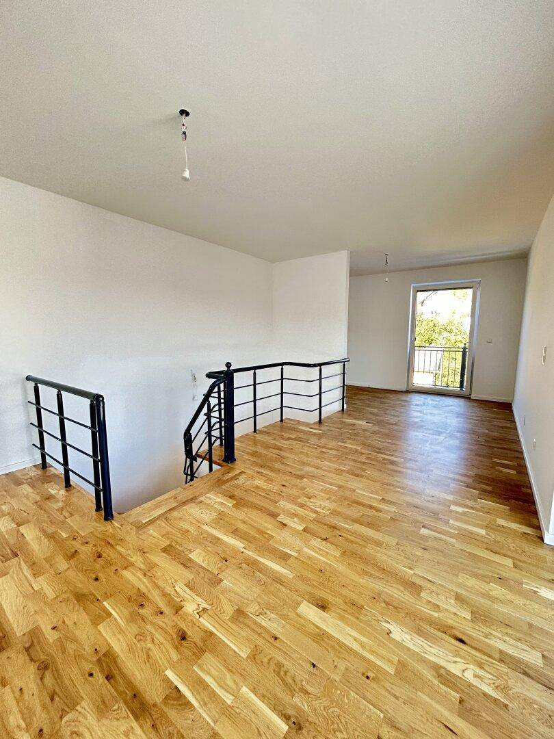 Geräumiger Wohnbereich im Obergeschoss mit Holzboden und Treppenzugang.