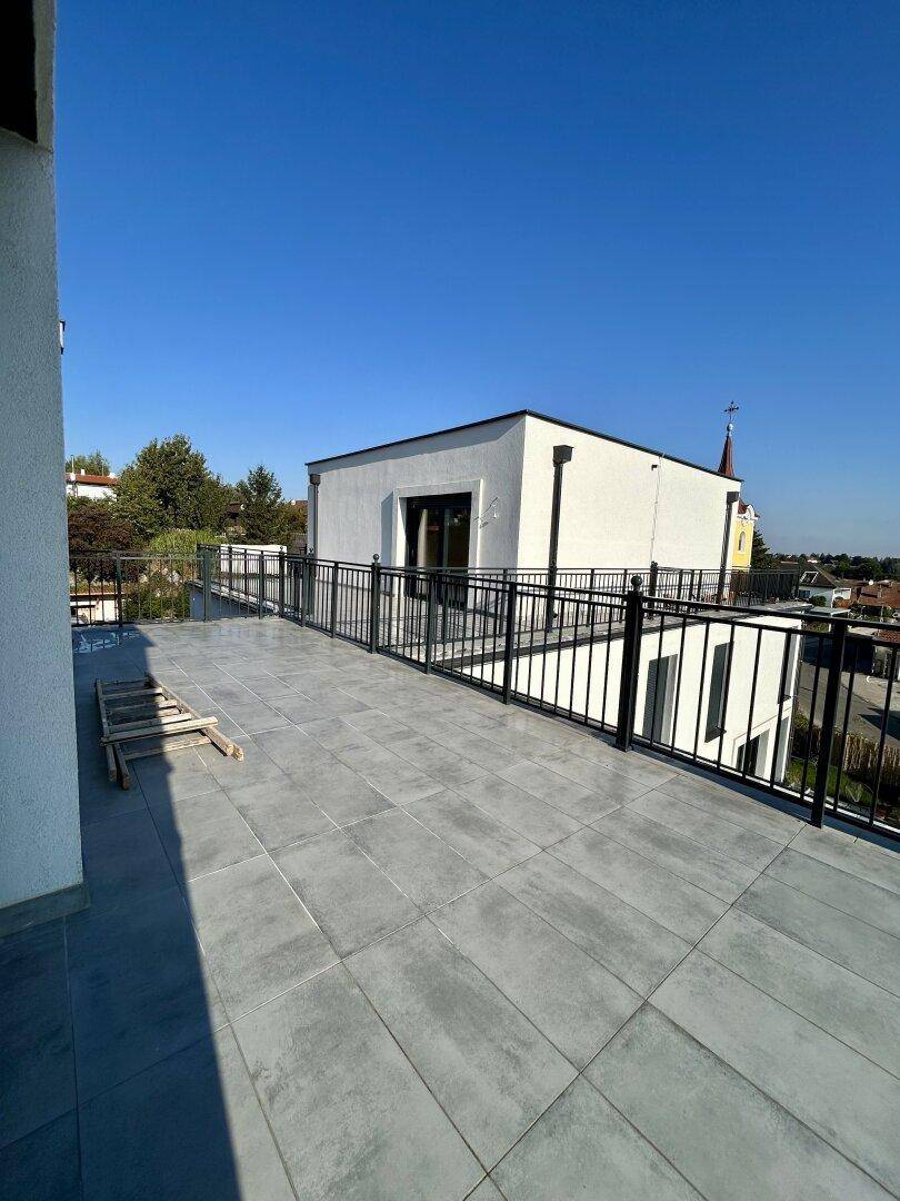 Große, geflieste Dachterrasse mit schwarzem Geländer und Blick auf die Umgebung.