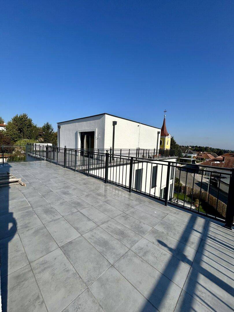 Weitläufige Dachterrasse mit grauen Fliesen und Blick auf die umliegenden Gebäude.