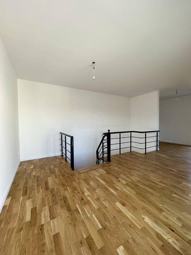 Geräumiger Wohnbereich im Obergeschoss mit Holzboden und Treppenzugang.