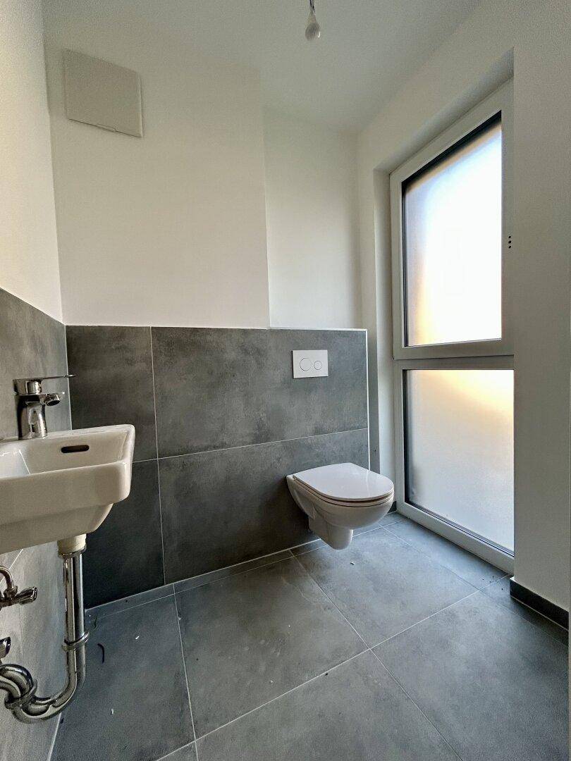 Kleines Gäste-WC mit modernen grauen Fliesen, wandhängendem WC und Fenster.