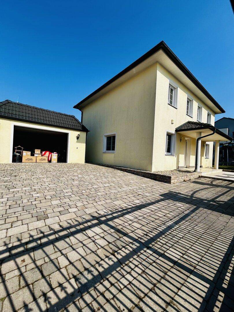 Einfamilienhaus mit separater Garage und gepflasterter Zufahrt unter strahlend blauem Himmel.