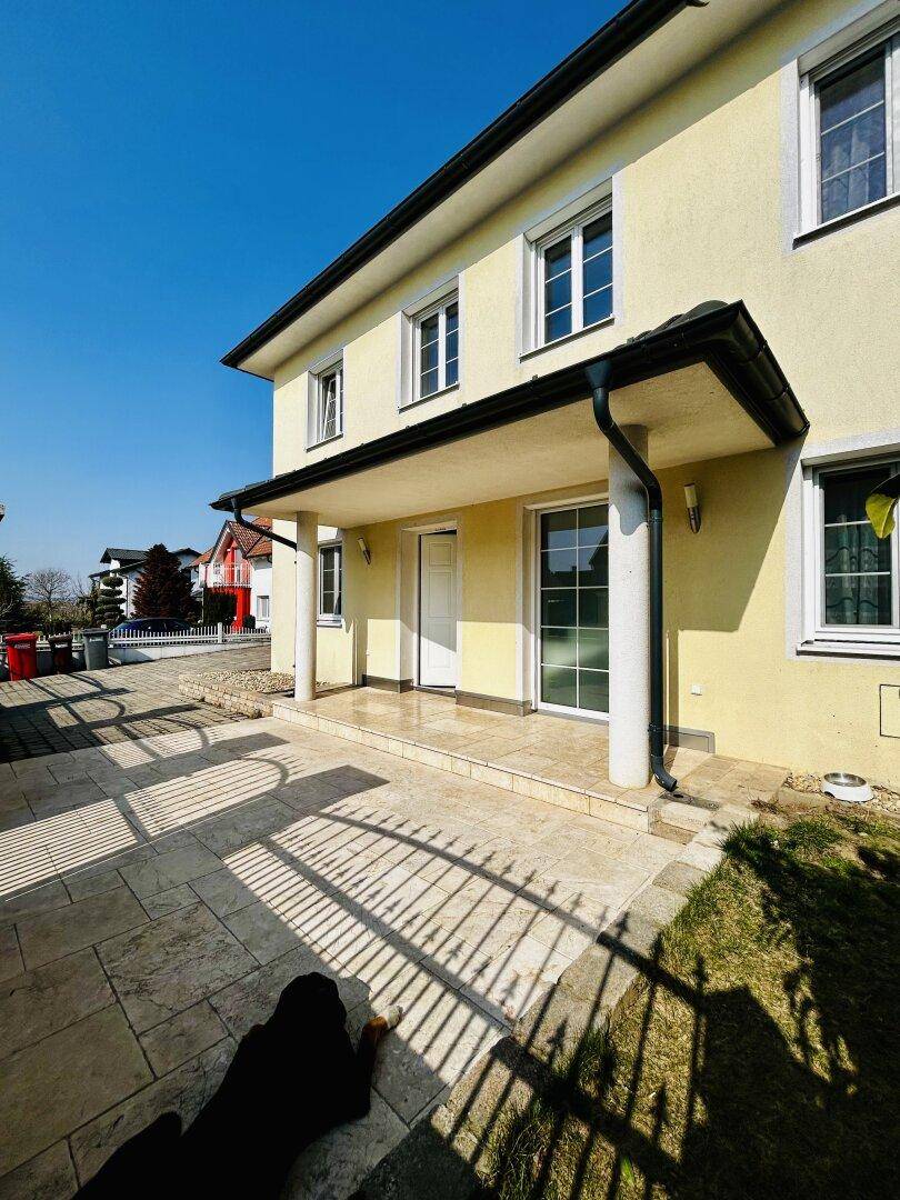 Überdachter Eingangsbereich mit gefliester Fläche und Zugang zum Haus, sonnendurchflutet.