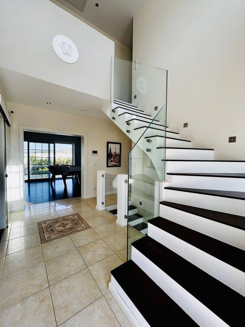 Moderner Eingangsbereich mit eleganter Glasgeländer-Treppe und Fliesenboden.