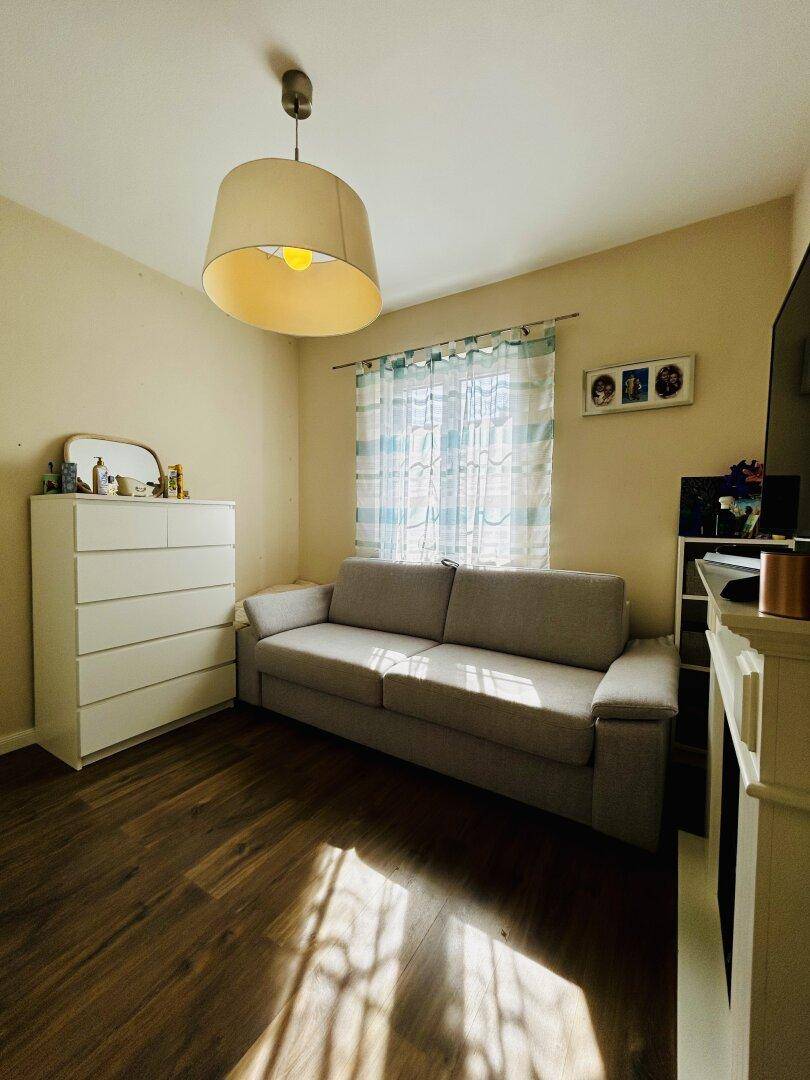 Helles Schlafzimmer mit Sofa, Kommode und Holzboden, ideal als Gästezimmer.