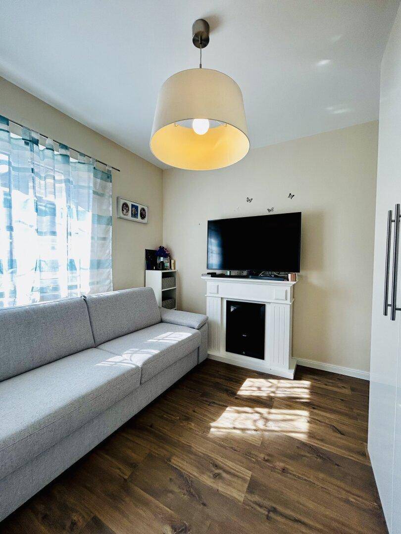 Gemütliches Schlafzimmer mit Sofa, Fernseher und Holzboden, gut beleuchtet.