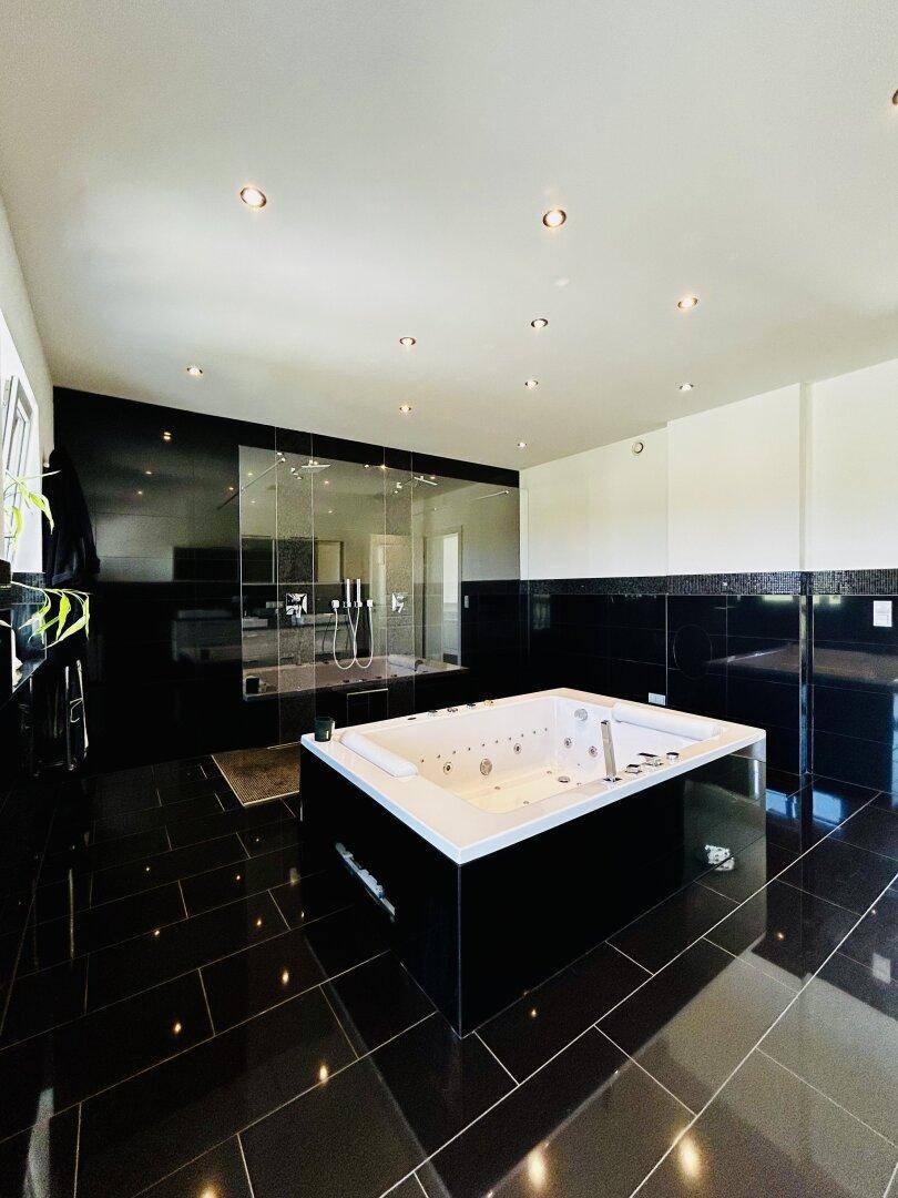 Luxuriöses Badezimmer mit Whirlpool, großer Dusche und eleganten schwarzen Fliesen.