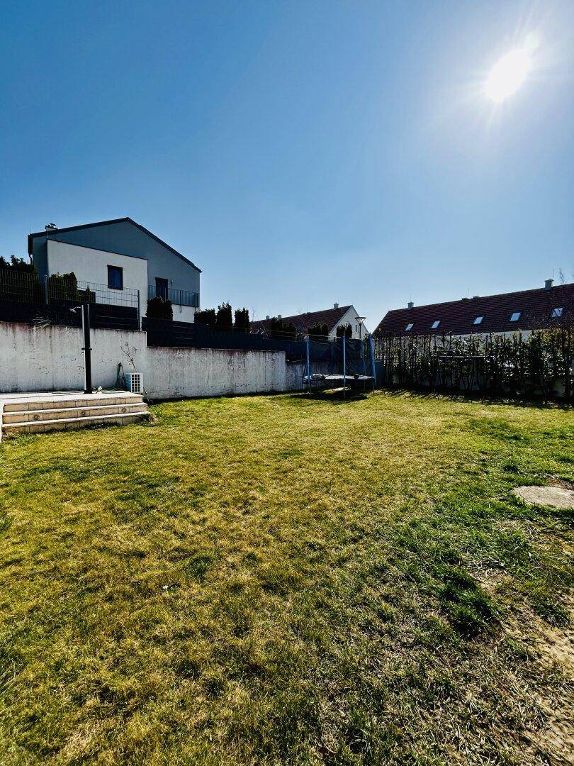 Großer, sonniger Garten mit Rasenfläche und Trampolin, ideal für Familien.