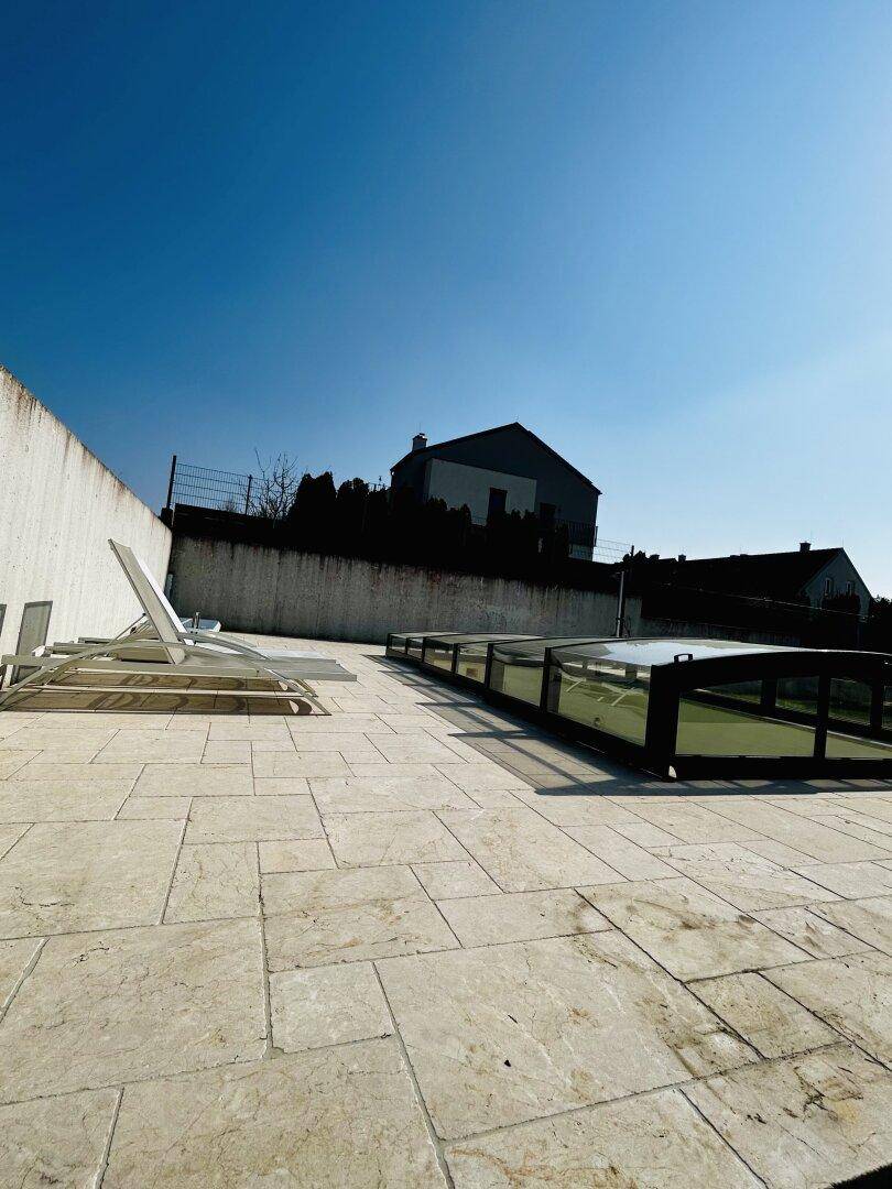 Große, sonnige Terrasse mit hellen Fliesen und Liegestühlen, ideal zum Entspannen im Freien.