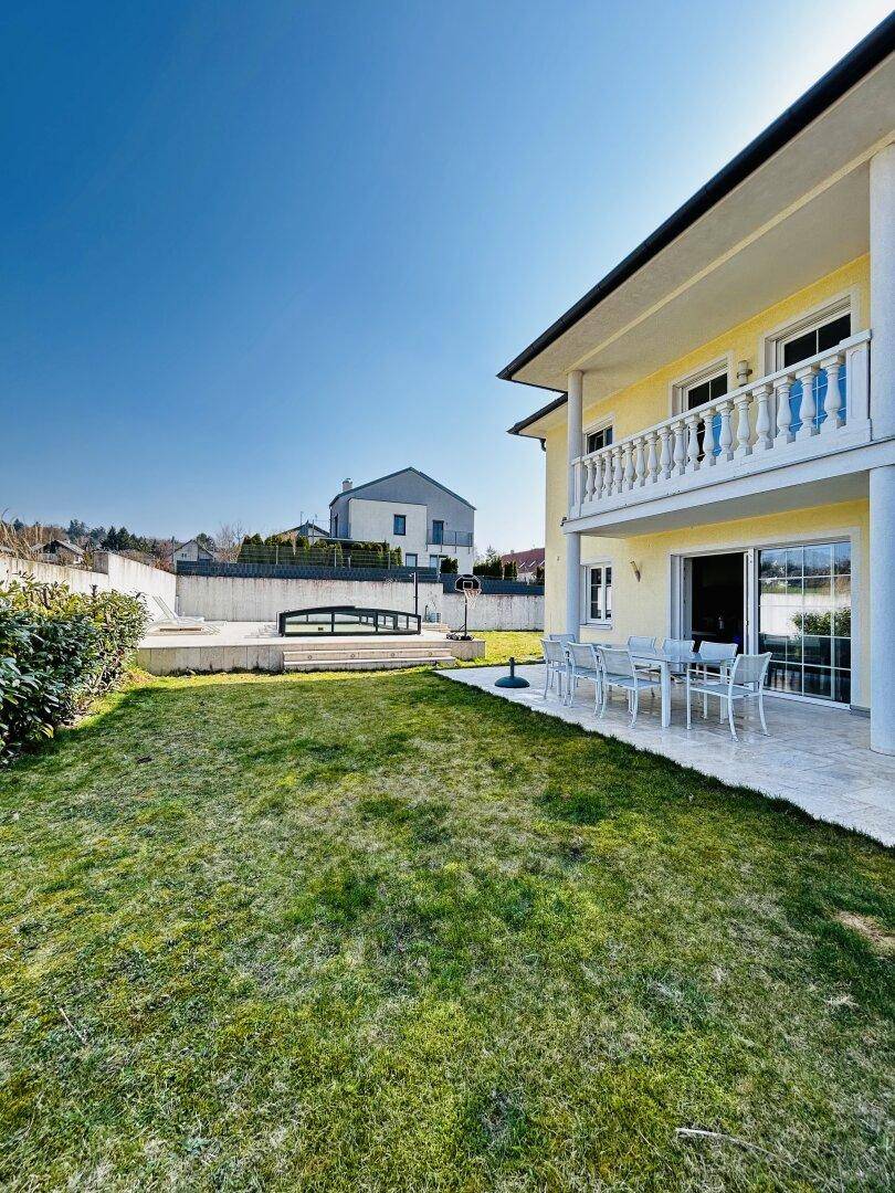 Seitlicher Blick auf das Haus mit großem Garten, Terrasse und einem kleinen Poolbereich im Hintergrund.