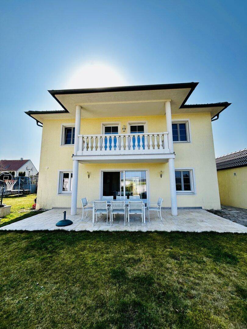 Rückseite eines Einfamilienhauses mit großer Terrasse, Rasenfläche und Balkon im Obergeschoss.