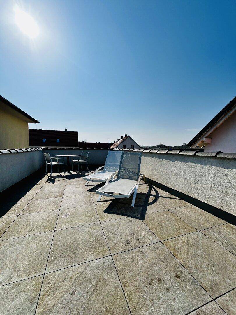 Sonniger Dachterrassenbereich mit Fliesenboden, Sitzgelegenheiten und weitem Blick über die Dächer.