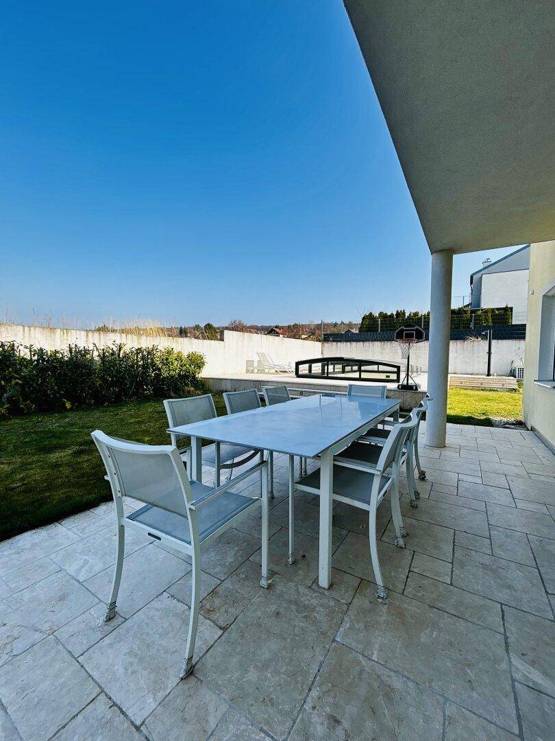 Geräumige Terrasse mit Esstisch und Stühlen, angrenzend an einen gepflegten Gartenbereich.