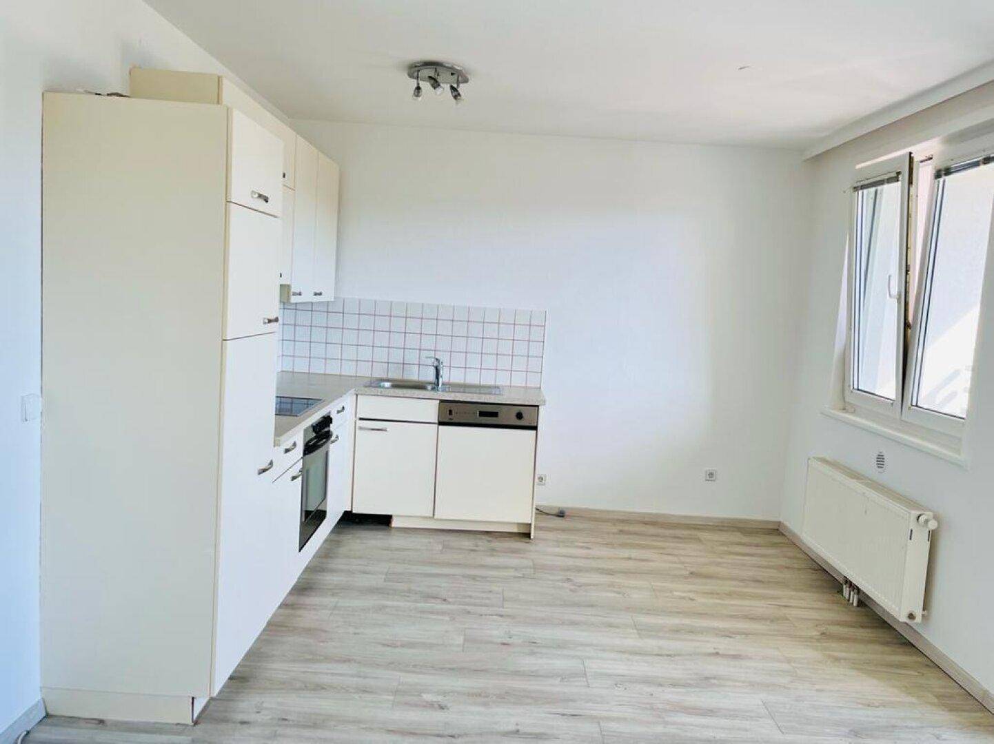 Helle Einbauküche mit weißen Schränken, Laminatboden und Fenster für natürliches Licht.