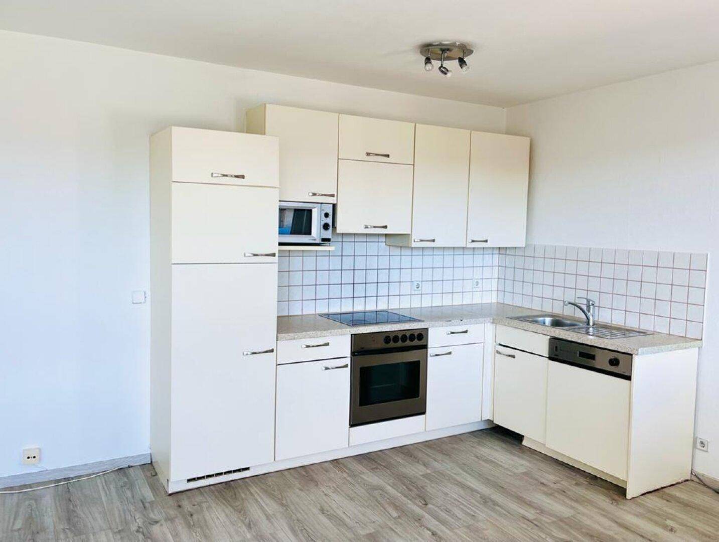 Funktionale Einbauküche mit weißen Fronten, integrierten Geräten und hellem Laminatboden.