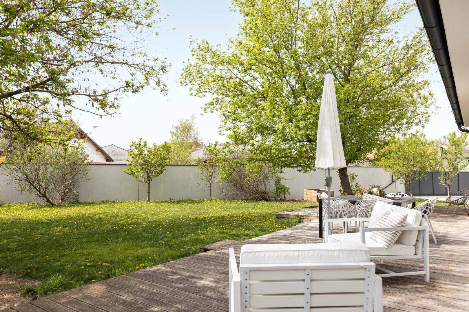 Großzügige Holzterrasse mit modernen Gartenmöbeln und Sonnenschirm im Grünen.
