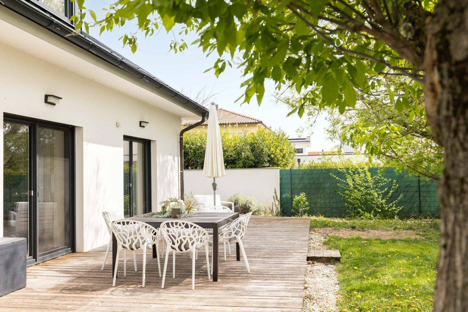 Hinteransicht des Hauses mit großer Holzterrasse, Essbereich und Blick in den Garten.