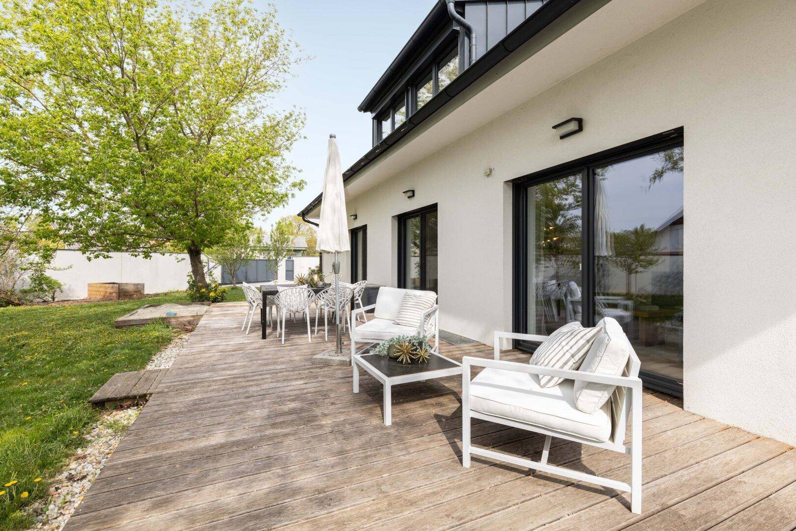 Großzügige Holzterrasse mit modernen Gartenmöbeln und Sonnenschirm im Grünen.