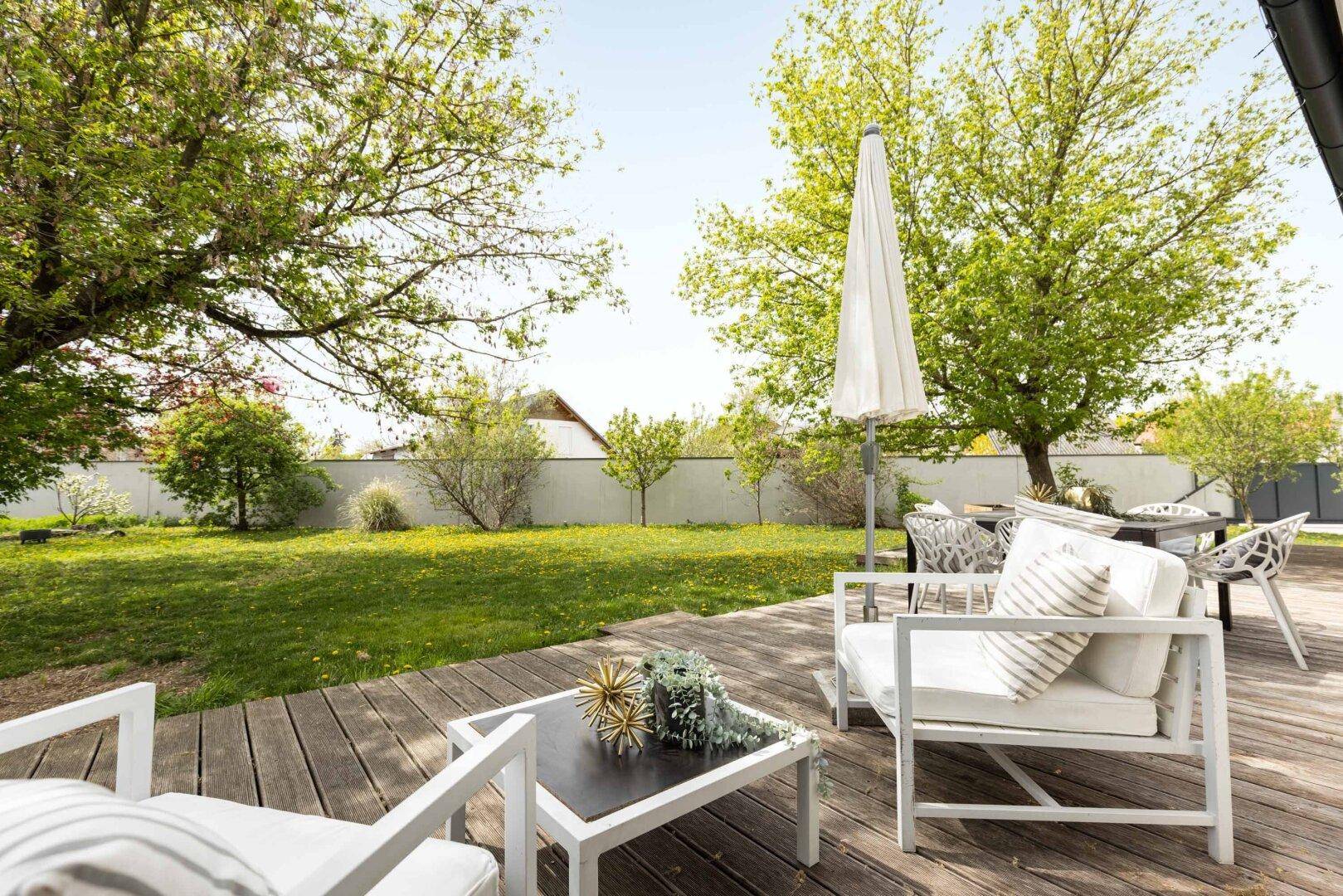Großzügige Holzterrasse mit modernen Gartenmöbeln und Sonnenschirm im Grünen.