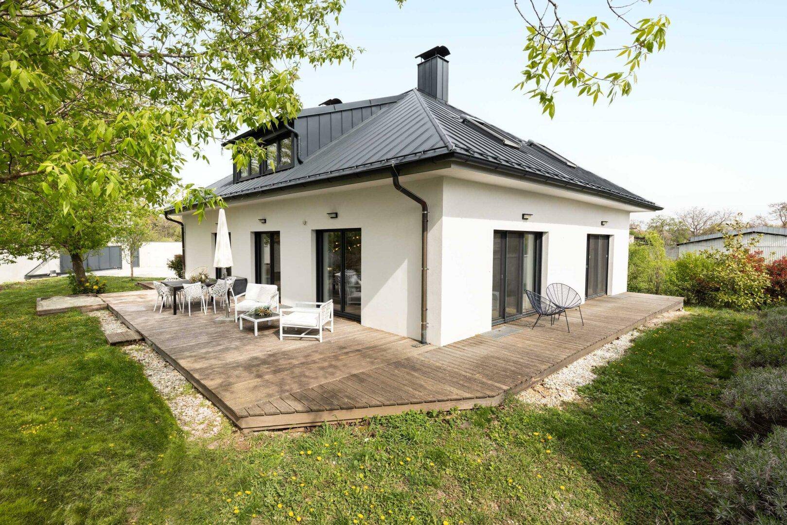Seitenansicht des Hauses mit großer Holzterrasse und gepflegtem Gartenbereich.