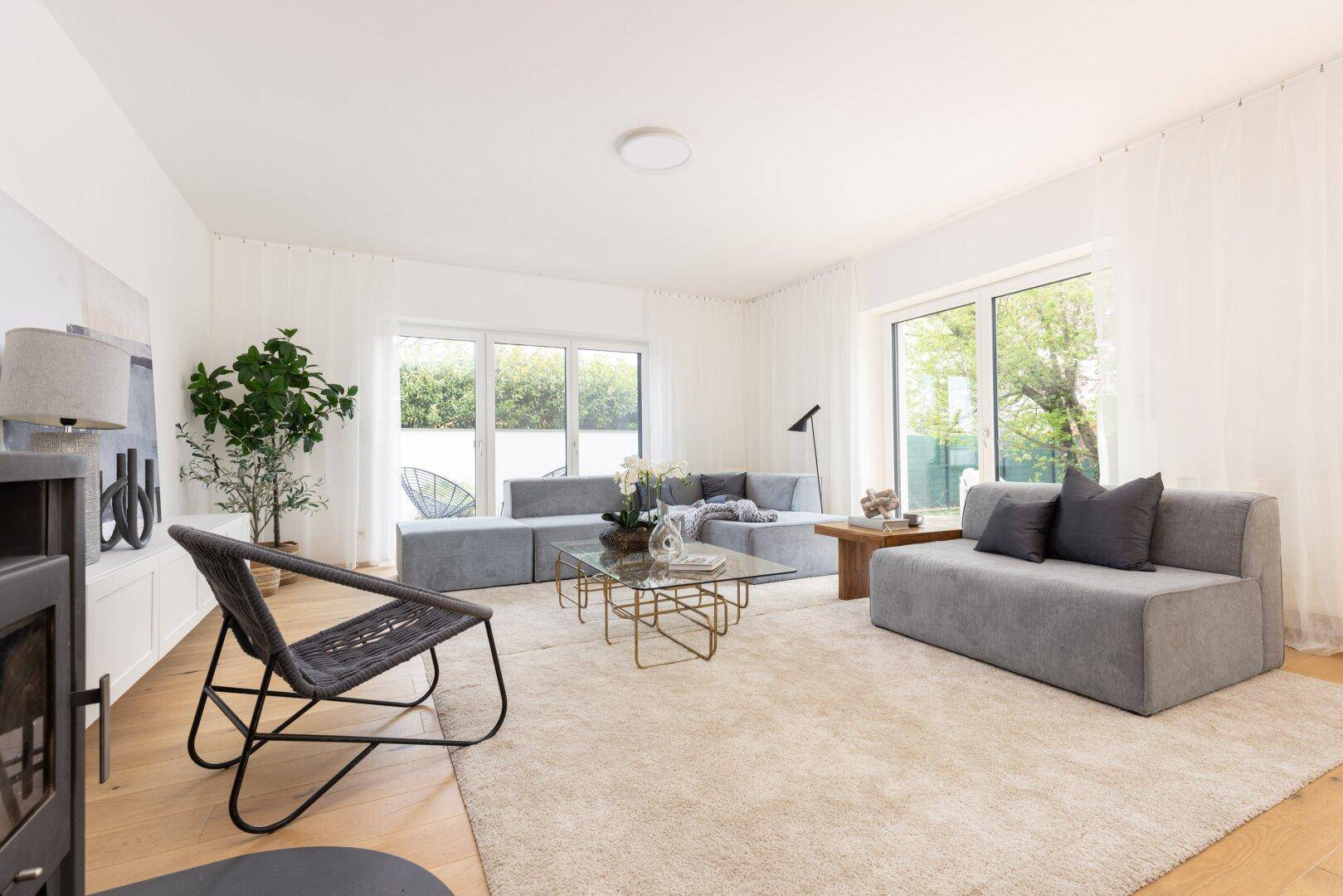 Geräumiges Wohnzimmer mit bequemen grauen Sofas, Teppich und großen Fenstern.