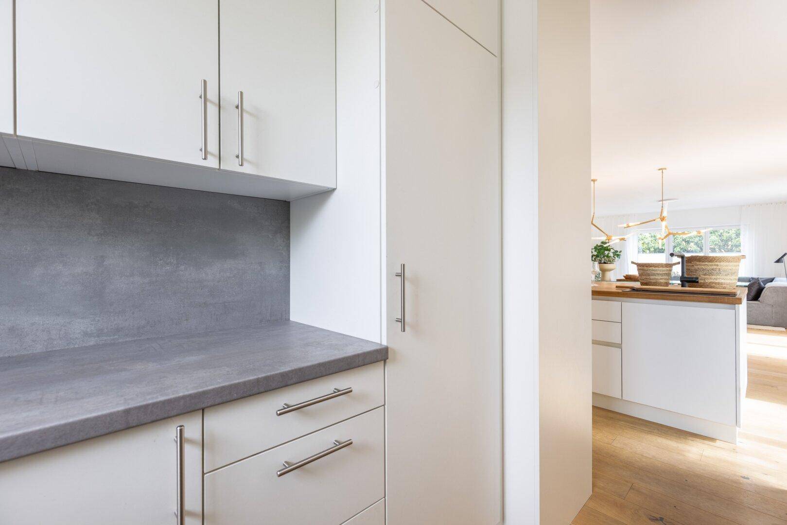 Detailansicht der weißen Küchenschränke und grauen Arbeitsplatte mit Blick in den offenen Wohnbereich.