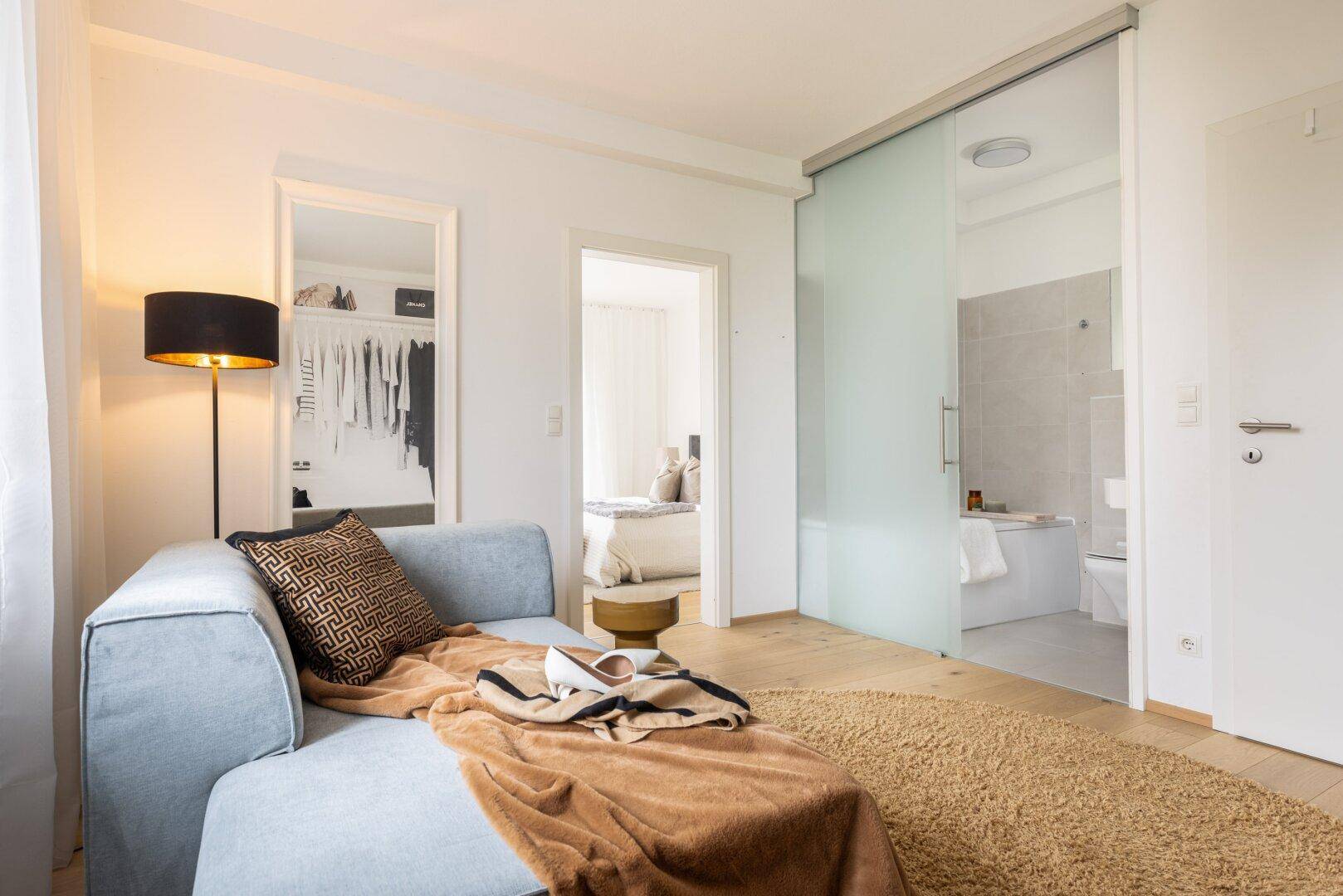 Gemütlicher Bereich mit Chaiselongue, Zugang zu begehbarem Kleiderschrank und Badezimmer mit Glasschiebetür.