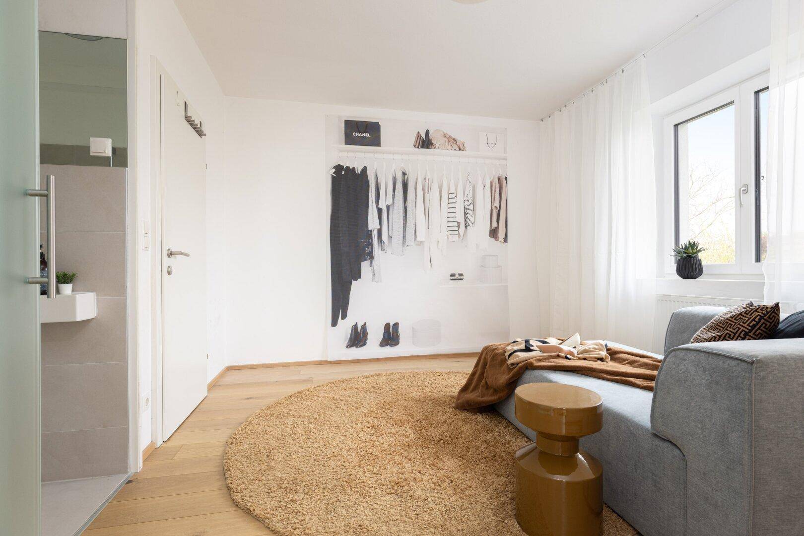 Lounge-Bereich mit Chaiselongue, rundem Teppich und stilvoller Kleiderschrank-Grafik.