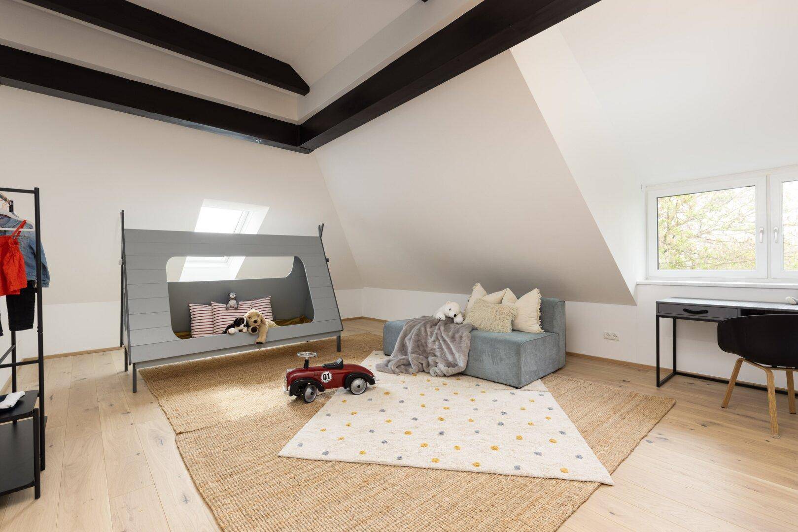 Helles Kinderzimmer im Dachgeschoss mit sichtbaren Holzbalken und Spielbereich.