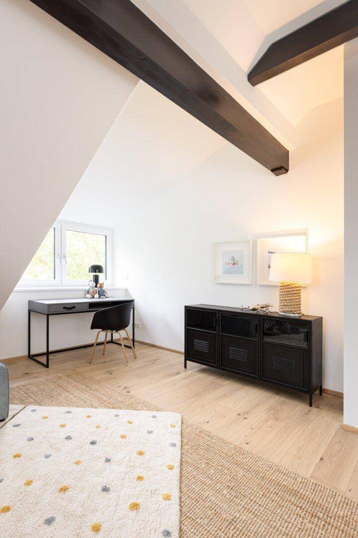 Arbeitsbereich im Dachgeschoss mit Schreibtisch, Fenster und sichtbaren Holzbalken.