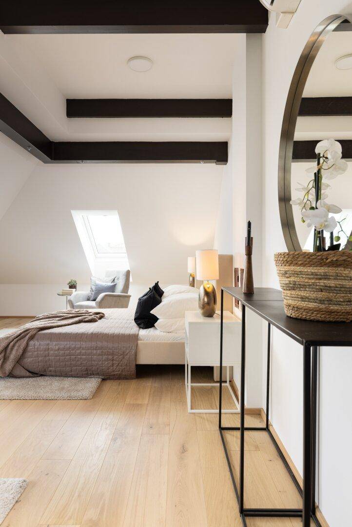 Schlafzimmer im Dachgeschoss mit Holzbalken, Bett und modernem Konsolentisch.