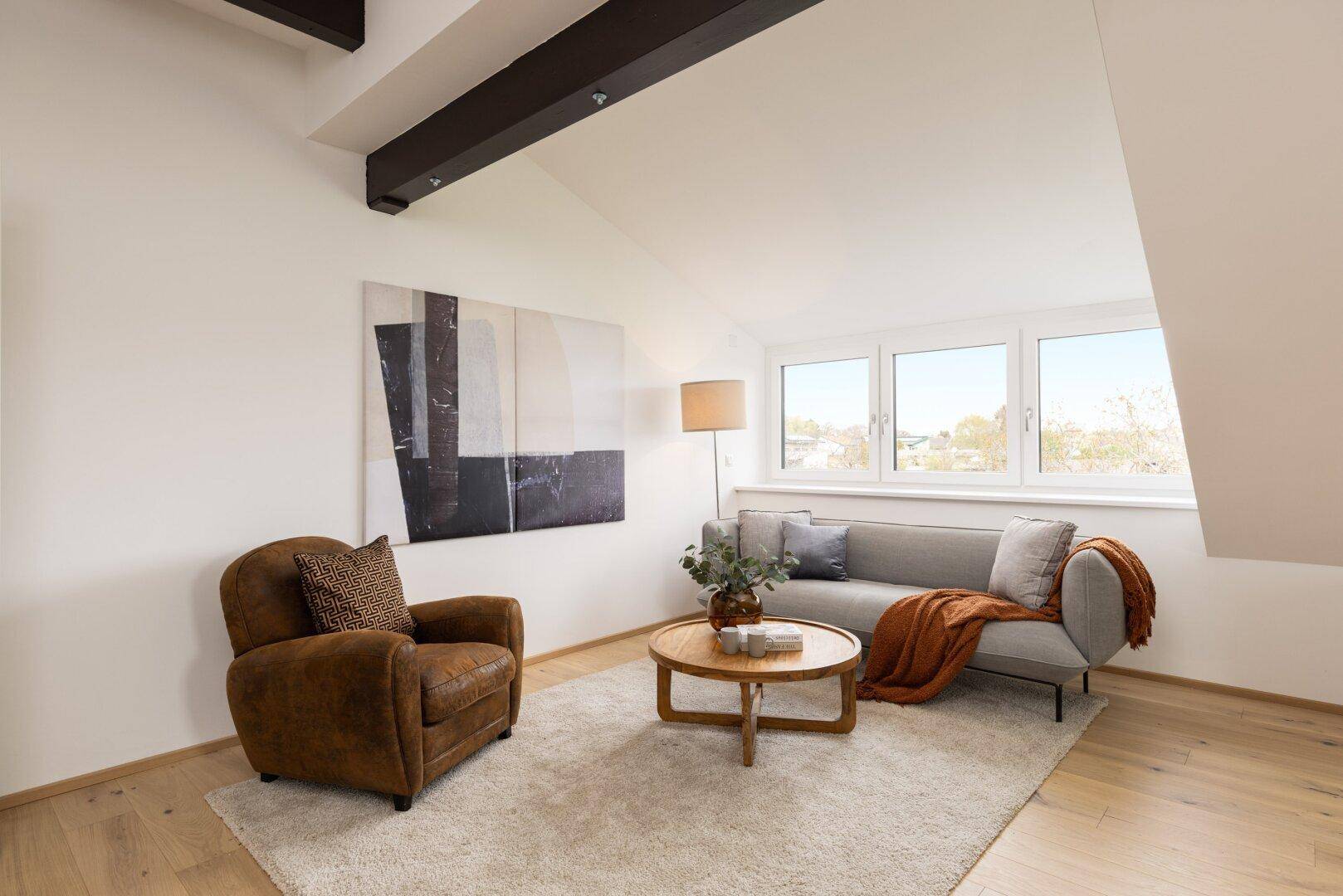 Gemütliches Wohnzimmer im Dachgeschoss mit Sofa, Sessel und großem Fenster.
